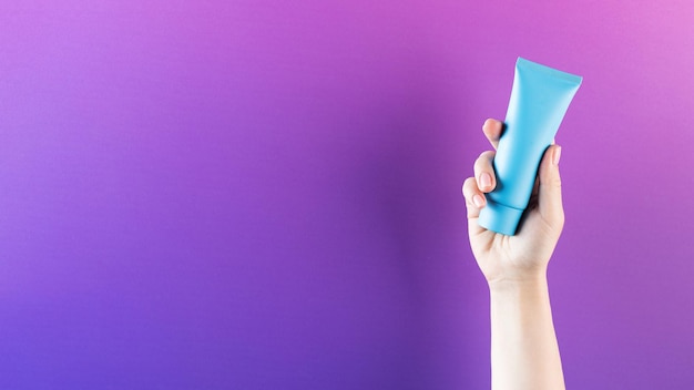 Mockup di un tubo blu con un prodotto cosmetico in una mano femminile su sfondo viola Spazio di copia Banner