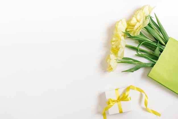 Mockup di una borsa della spesa di carta con fiori di tulipano adagiati su uno sfondo bianco Vendita di Pasqua primaverile Il concetto di rispetto per l'ambiente e l'assenza di rifiuti