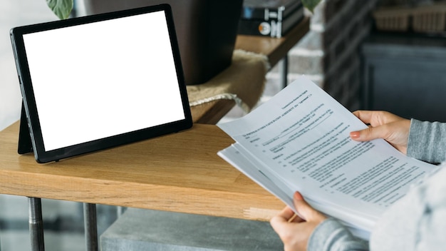 Mockup digitale per il lavoro a casa che controlla i documenti mani femminili che tengono il contratto cartaceo seduto con il tablet
