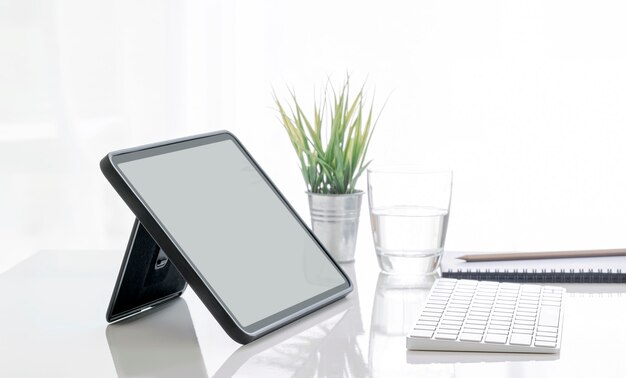 Mockup tablet schermo vuoto su supporto e tastiera sul tavolo bianco, sfondo luminoso luminoso.