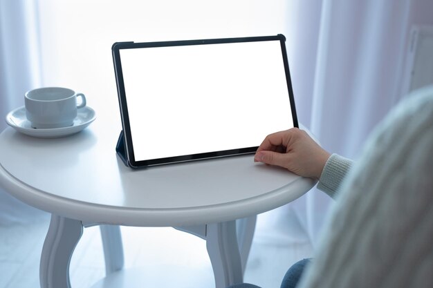 Mockup tablet su tavolo bianco Donna irriconoscibile che utilizza tablet digitale con schermo vuoto seduto al tavolo con mockup di caffè per app mobile o sito Web Modello per pubblicità online