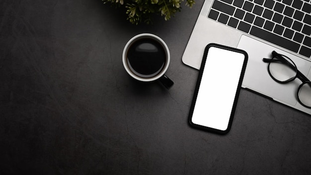 Mockup telefono cellulare con schermo bianco computer portatile tazza di caffè e occhiali da vista sul tavolo nero