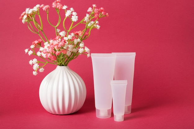 Mockup tre tubi traslucidi bianchi per crema accanto a un vaso con fiori su uno sfondo di colore magenta