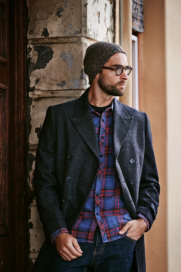 Foto moda all'aperto o uomo da un muro pensando a abiti casuali stile o cappotto tagliente per un abito invernale moderno viaggiare modello cool o persona elegante in una città urbana in berretto o giacca alla moda in italia