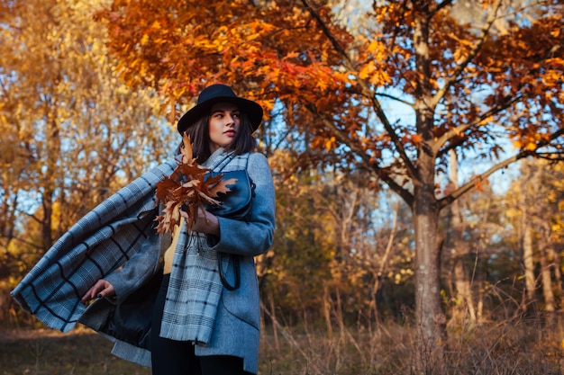 Moda autunno. Giovane donna che cammina nel parco che indossa attrezzatura alla moda e che tiene borsa. Abbigliamento e accessori