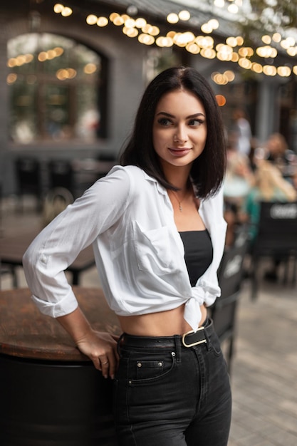 Moda bella donna con eleganti jeans neri e camicia bianca si trova in città