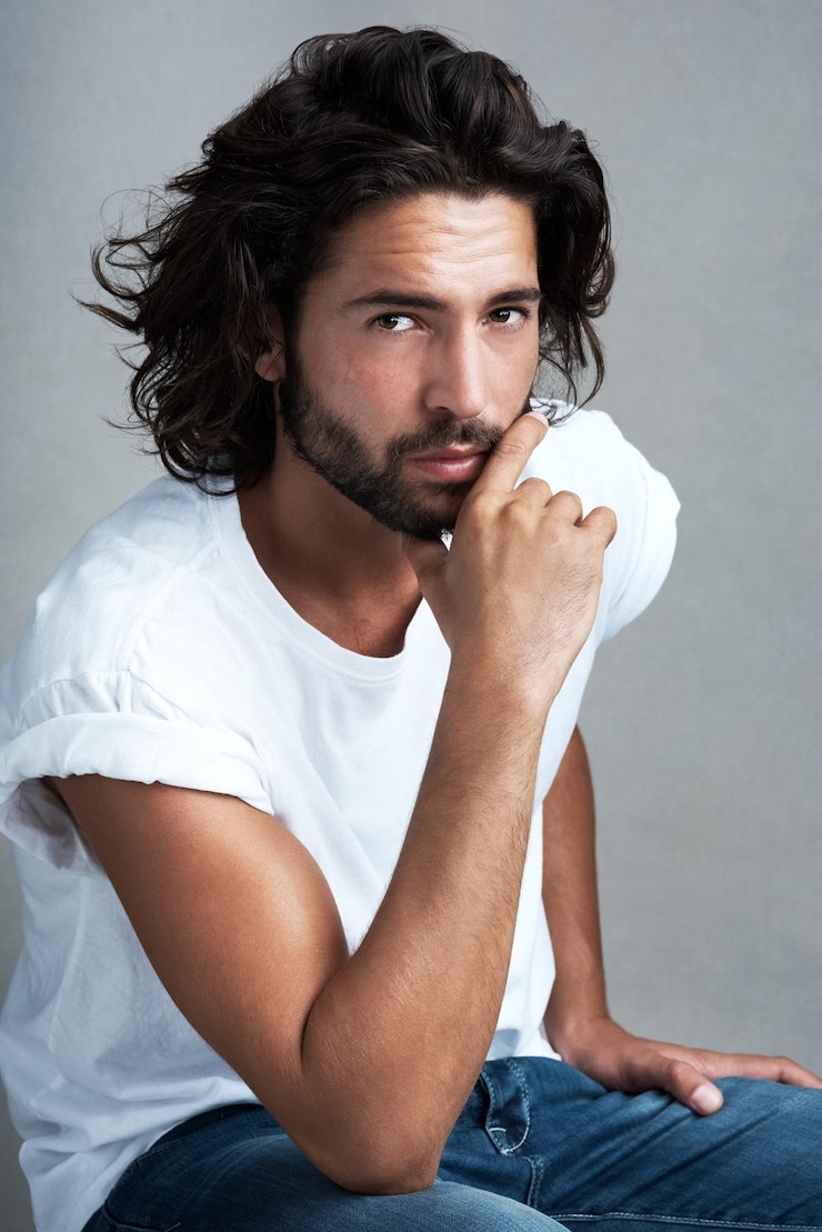 Foto moda casuale e ritratto di uomo in studio con fiducia abbigliamento di designer e rilassarsi sulla sedia jeans orgoglio e cool modello maschile su uno sgabello con stile creativo elegante estetica o sfondo grigio