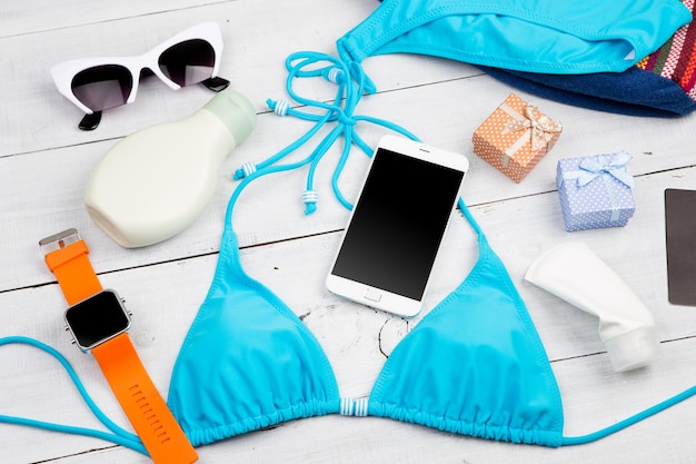 Moda donna estiva con borsa da bagno blu smart phone occhiali da sole crema solare smart watch scatole regalo su scrivania in legno bianco