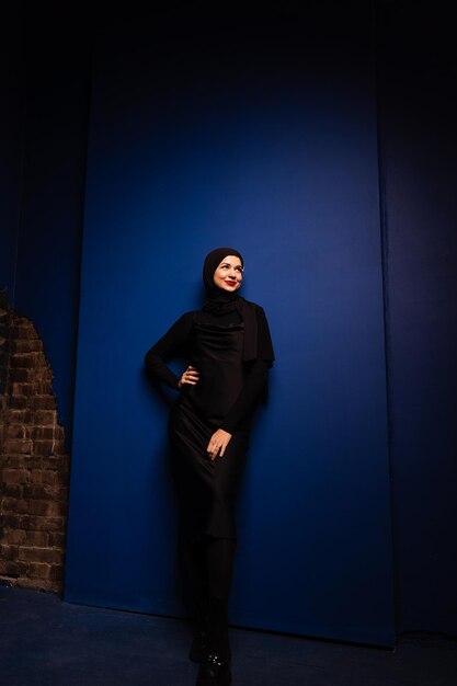 Moda donna musulmana in hijab nero è in posa su sfondo blu in studio Modello caucasico professionale