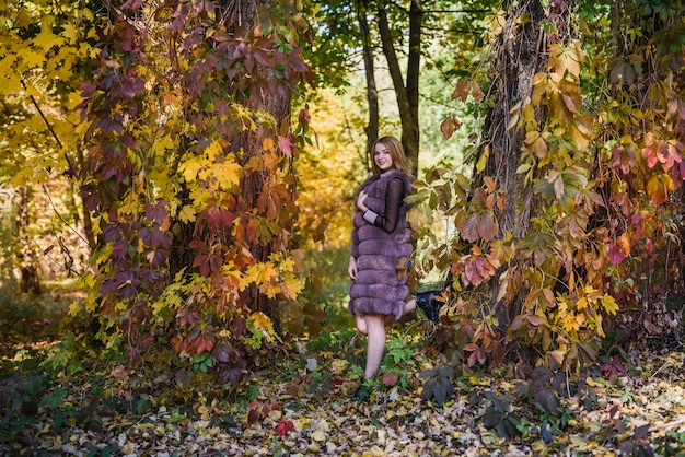 Moda donna. Ragazza sorridente in pelliccia posan nel parco autunnale con alberi ed edera