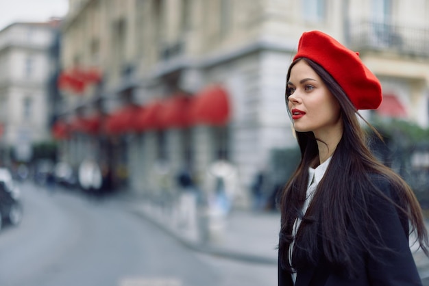 Moda donna ritratto bellezza in piedi sulla strada di fronte alla città in abiti eleganti con labbra rosse e berretto rosso viaggio colore cinematografico retrò stile vintage stile di vita moda urbana