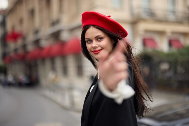 Moda donna sorriso con i denti in piedi sulla strada di fronte al turista della città seguimi vestiti eleganti con labbra rosse e berretto rosso viaggio colore cinematografico retrò stile vintage moda urbana