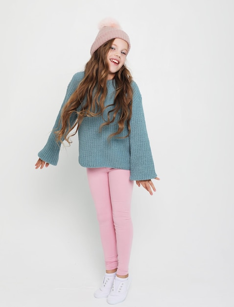 Moda infantile e concetto di persone Bambina con cappello rosa e maglione blu che salta sullo sfondo bianco