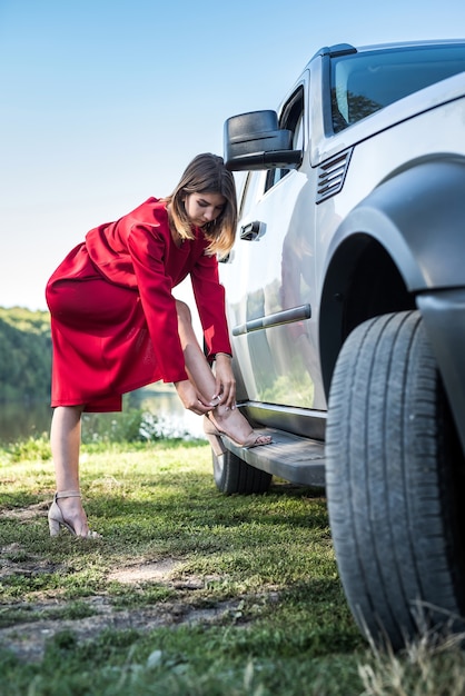 Moda ragazza in elegante abito rosso in piedi vicino alla sua auto moderna e relax ar nature