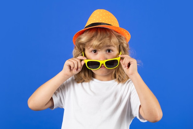 Moda ritratto di bambino stupito in maglietta cappello estivo e occhiali da sole su sfondo blu studio isolato