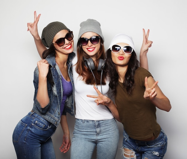 Moda ritratto di tre migliori amiche ragazze hipster sexy alla moda, su superficie grigia. Tempo felice per il divertimento.