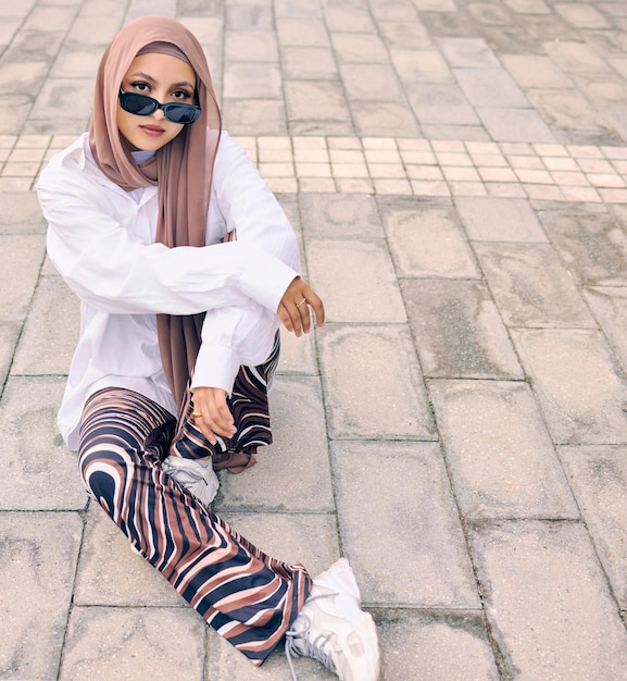 Moda ritratto o città con una donna musulmana all'aperto in occhiali da sole e una sciarpa per la religione islamica in stile urbano o arabo e una giovane persona saudita alla moda seduta fuori in abiti moderni con spazio