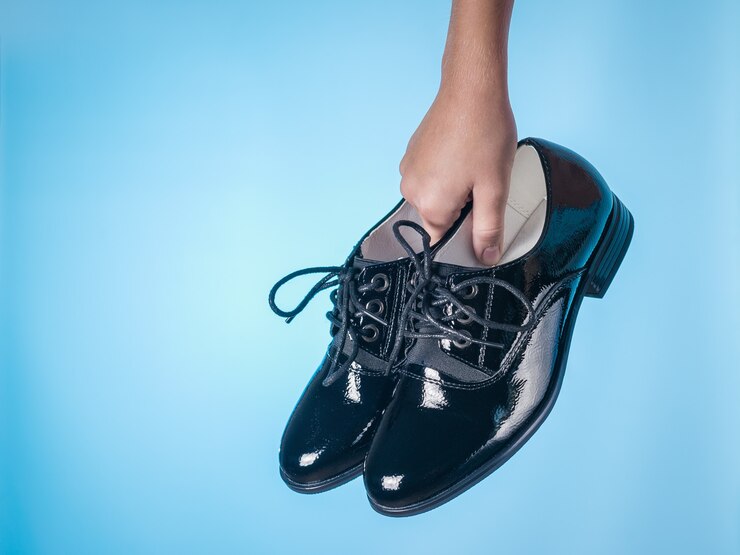 Moda scarpe da donna con lacci in mano del bambino sulla superficie blu. Scarpe da donna in pelle eleganti e alla moda.