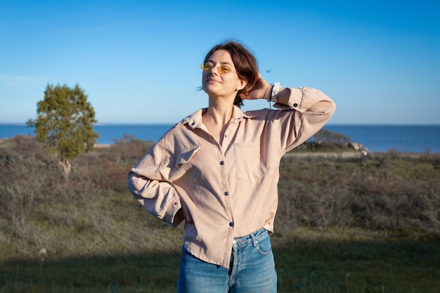 Moda stile di vita ritratto di giovane donna alla moda vestita in camicia e jeans ridendo, sorridendo, in posa sulla spiaggia