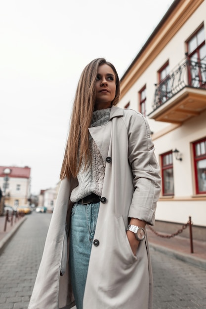 modella di una giovane donna con un trench e un maglione vintage lavorato a maglia cammina per strada