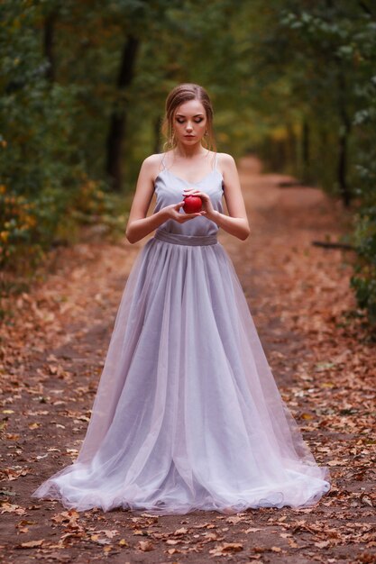 modella in un abito delicato nella foresta. sposa. nelle sue mani c'è una mela rossa.