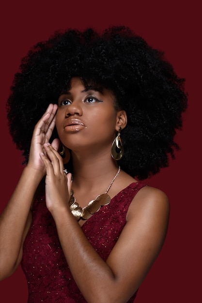 modella nera con grandi capelli afro mostra grandi orecchini e collana dorata con vestito rosso