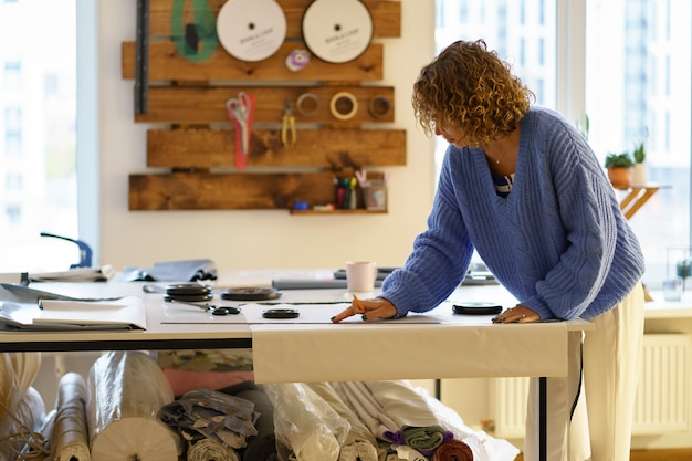 Modelli di carta da bozza di sarta su tessuto con gesso e righello designer di vestiti lavorano in studio