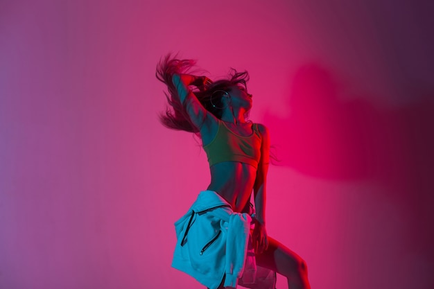 Modello alla moda della giovane donna in vestiti alla moda della gioventù che ballano nello studio con il colore rosa neon luminoso stupefacente nello stile della discoteca. Ballerino moderno esile della ragazza sexy che posa all'interno con luce multicolore.