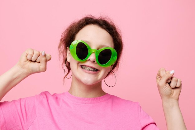 Modello alla moda della ragazza dell'adolescente con il gesto della decorazione degli occhiali verdi con le sue mani