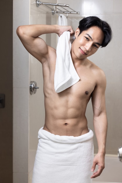 Modello asiatico del giovane bell'uomo con l'asciugamano in bagno