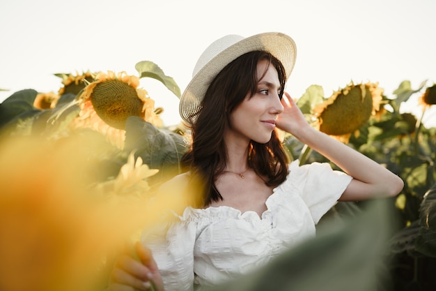 Modello attraente della giovane donna che posa nel campo dei girasoli