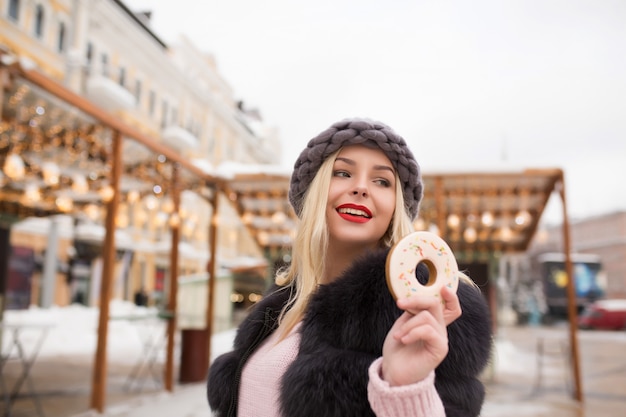Modello biondo alla moda che tiene un delizioso biscotto allo zenzero contro la decorazione leggera alla fiera di Natale a Kiev