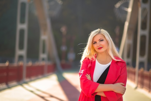 Modello biondo alla moda con trucco luminoso che posa in cappotto rosso alla via