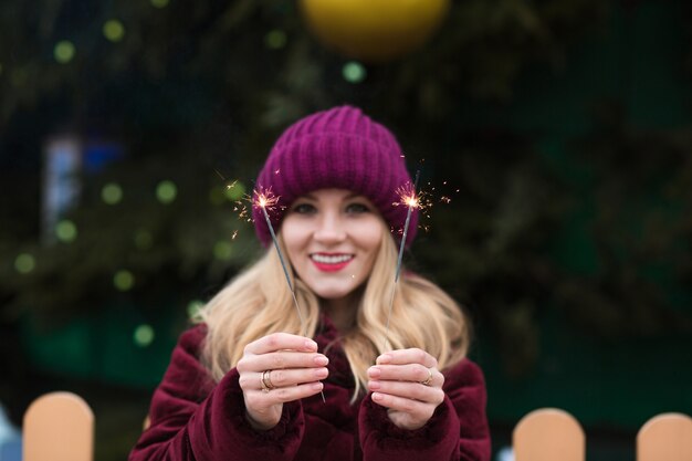 Modello biondo allegro che tiene le luci di Bengala incandescenti all'albero di Natale principale a Kiev. Effetto sfocatura