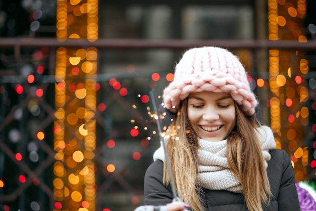 Modello biondo emotivo che indossa abiti invernali per festeggiare il nuovo anno in strada con le stelle filanti. Spazio per il testo