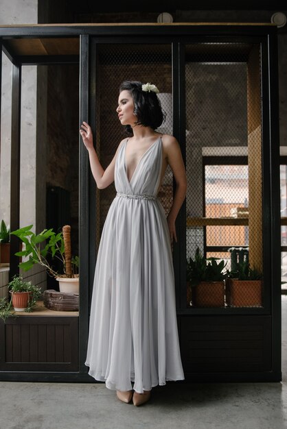 Modello che propone in un abito da sposa lungo bianco al chiuso dalla finestra.