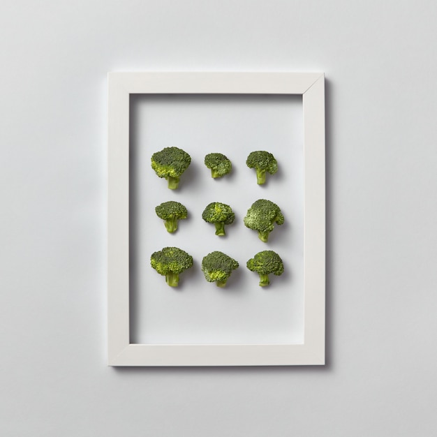 Modello creativo di broccoli organici appena raccolti naturali in una cornice su un muro grigio chiaro, posto per il testo. Vista dall'alto. Concetto di cibo vegetariano.