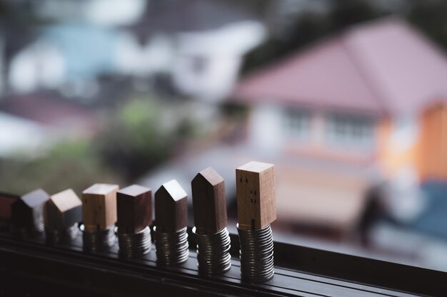 Modello della casa di legno e fila di soldi della moneta sulla tavola di legno con fondo blu-chiaro, Real Esta