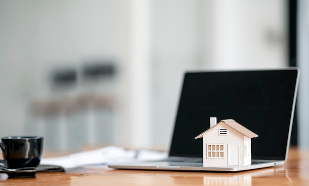 Modello della casa sul computer portatile sulla tavola di legno con lo spazio della copia, concetto del bene immobile.