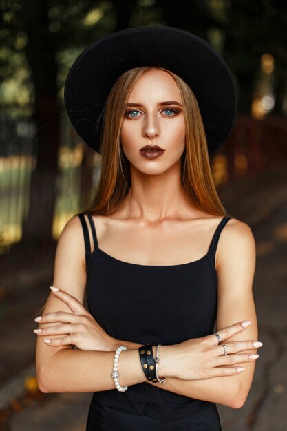 Modello di bella donna alla moda in cappello nero di moda nel parco