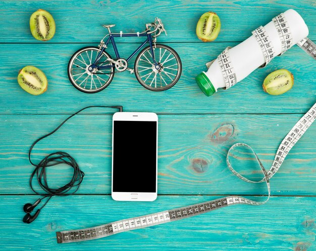 Modello di bicicletta cuffie smartphone kiwi bottiglia d'acqua e nastro centimetro sulla scrivania di legno blu