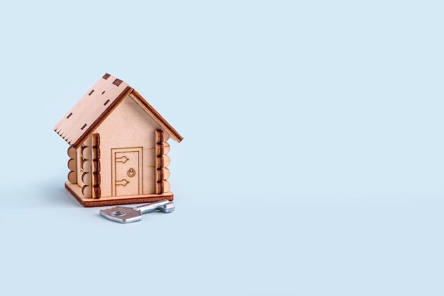 Modello di casa in legno e chiave su sfondo blu. Concetto di acquisto e vendita di case e immobili. Assicurazione casa, proprietà e mutuo. Copia spazio per il testo