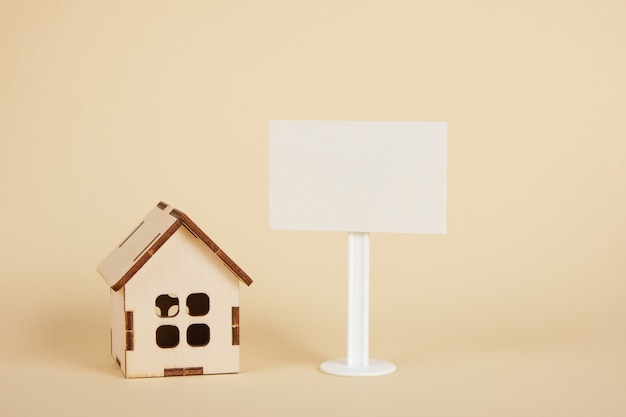 modello di casa in legno e segno bianco bianco su sfondo beige copia spazio concetto di bene immobile