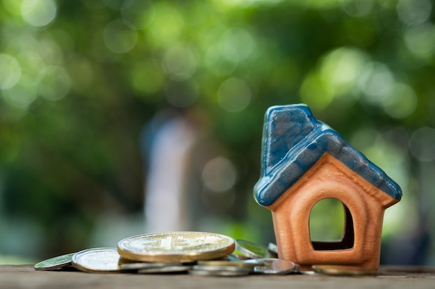 modello di casa in miniatura con monete su sfondo di legno