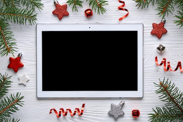 Modello di composizione di Natale. Tablet, ramoscelli di abete e decorazioni per l'albero di Natale su uno sfondo di legno chiaro. Vista dall'alto.