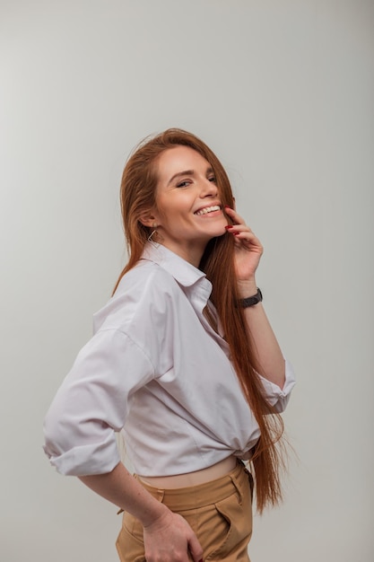 Modello di donna bella rossa felice con sorriso carino e capelli lunghi rossi in camicia bianca di moda in studio