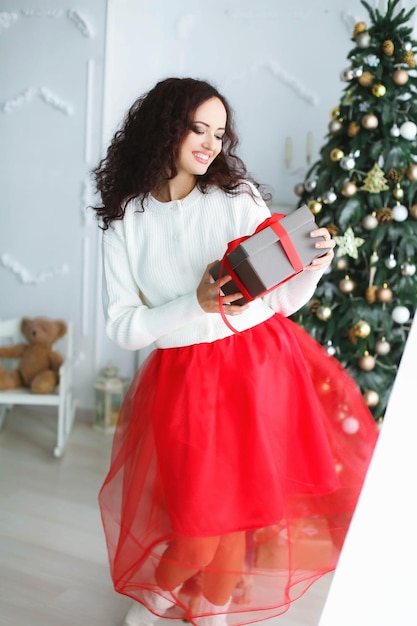 Modello di donna con un vestito rosso in uno studio fotografico con in mano un regalo di Capodanno