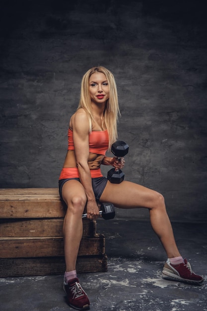 Modello di fitness femminile biondo in posa con manubri su scatole di legno in studio.