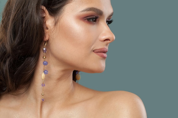 Modello di gioielli elegante e elegante donna bruna con capelli lunghi e ricci pelle sana e orecchini in primo piano