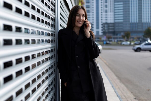 Modello di giovane donna europea che chiacchiera al telefono contro il muro dell'edificio